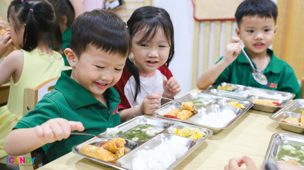 Nụ cười rạng rỡ của bé ICANDY Preschool trước khay cơm trưa đầy đủ rau xanh và bắp ngọt