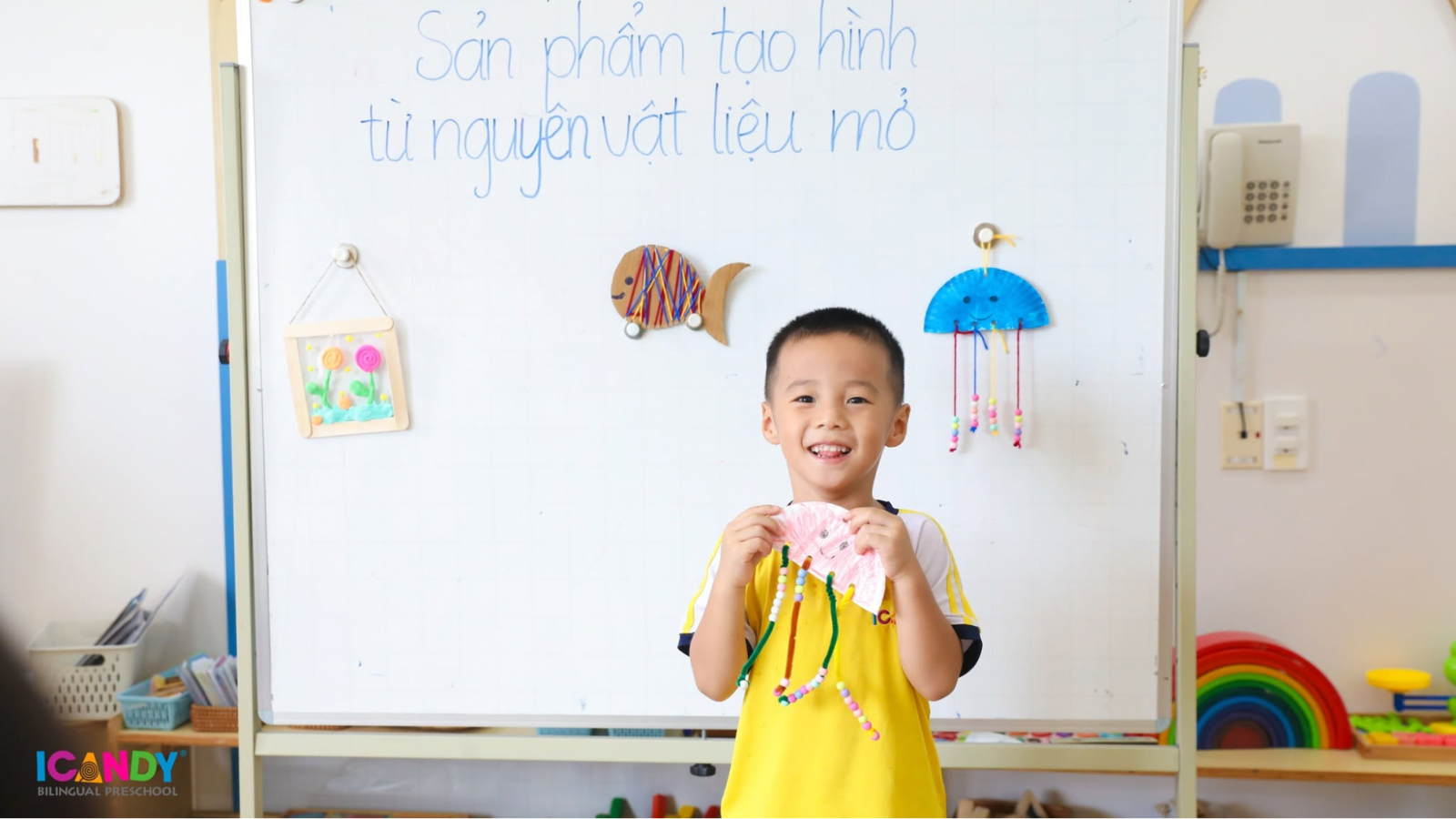 Nụ cười rạng rỡ của học sinh ICANDY Preschool bên tác phẩm thủ công sáng tạo do bé tự làm